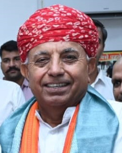 Close portrait of Bhagirath Choudhary in a red bandhani turban and an orange and blue stole, smiling