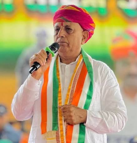Bhagirath Choudhary in a pink turban and tricolour stole speaking into a handheld microphone