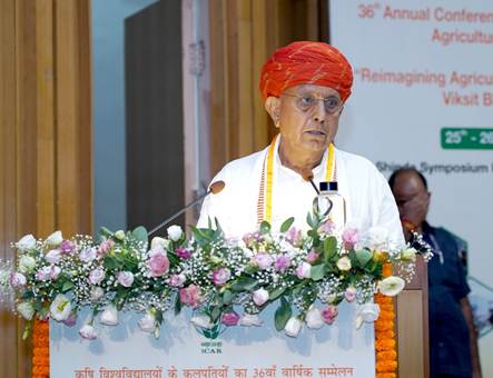 Bhagirath Choudhary speaks at a lectern decorated with roses and baby's breath, in front of a banner for the 36th Annual Conference of Vice-Chancellors of Agricultural Universities