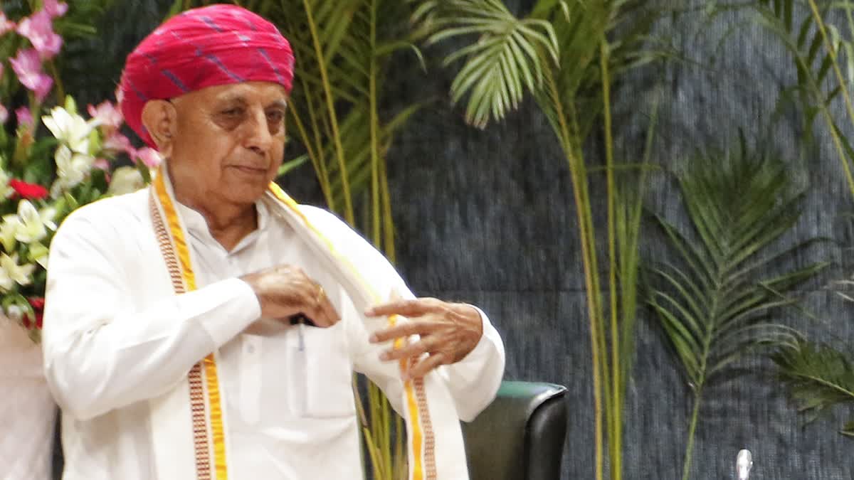 Bhagirath Choudhary adjusts his stole on a stage decorated with palms
