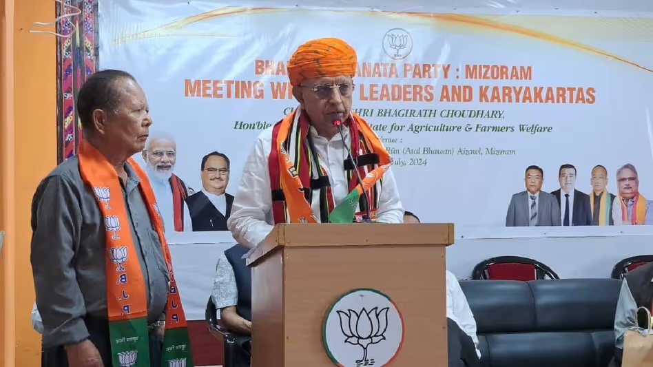 Bhagirath Choudhary, in an orange turban and Mizo stole, speaks at a podium before a banner reading BJP Mizoram, Meeting with Leaders and Karyakartas