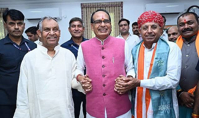Bhagirath Choudhary, in a red turban and blue stole, clasps hands with Union Agriculture Minister Shivraj Singh Chouhan, who wears a pink jacket, among colleagues in an office