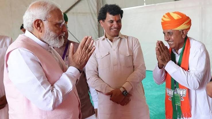 Bhagirath Choudhary, in an orange turban and BJP stole, greets Prime Minister Narendra Modi with folded hands; another man stands between them